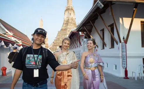 Tourists in traditional Thai costumes walking near Wat Arun in Bangkok.