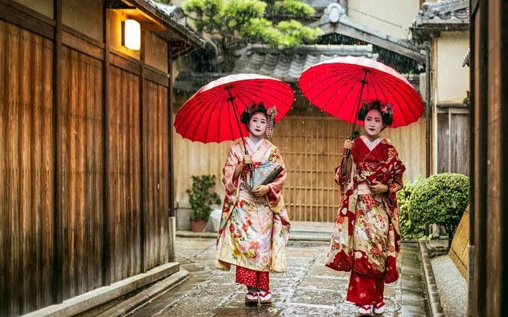 Geisha in traditional attire with red umbrellas on a Kyoto Gion street.