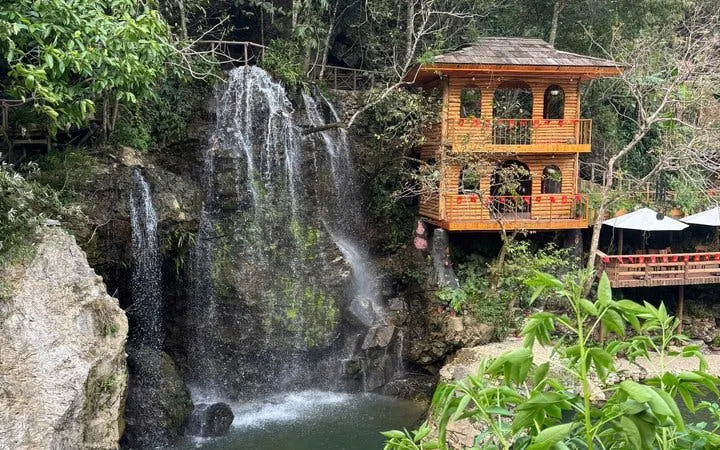 Waterfall beside wooden house in lush Sapa landscape during guided trek experience.