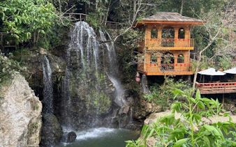 Waterfall beside wooden house in lush Sapa landscape during guided trek experience.