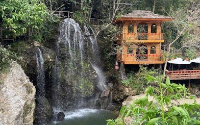 Waterfall beside wooden house in lush Sapa landscape during guided trek experience.