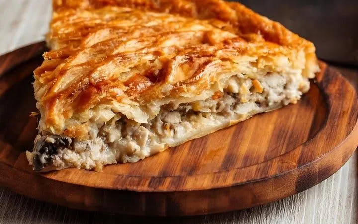 Slice of traditional Greek pie on a wooden plate, featured in Athens food walk.