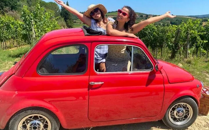 Vintage Fiat 500 with passengers in Chianti vineyard, Tuscany.