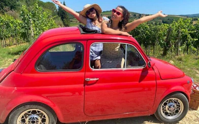Vintage Fiat 500 with passengers in Chianti vineyard, Tuscany.