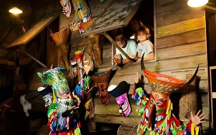 Performers in traditional costumes at Siam Niramit Phuket show, with colorful masks and wooden backdrop.