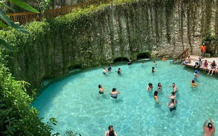 Visitors swimming in a hidden cenote surrounded by lush greenery, Punta Cana day tour.