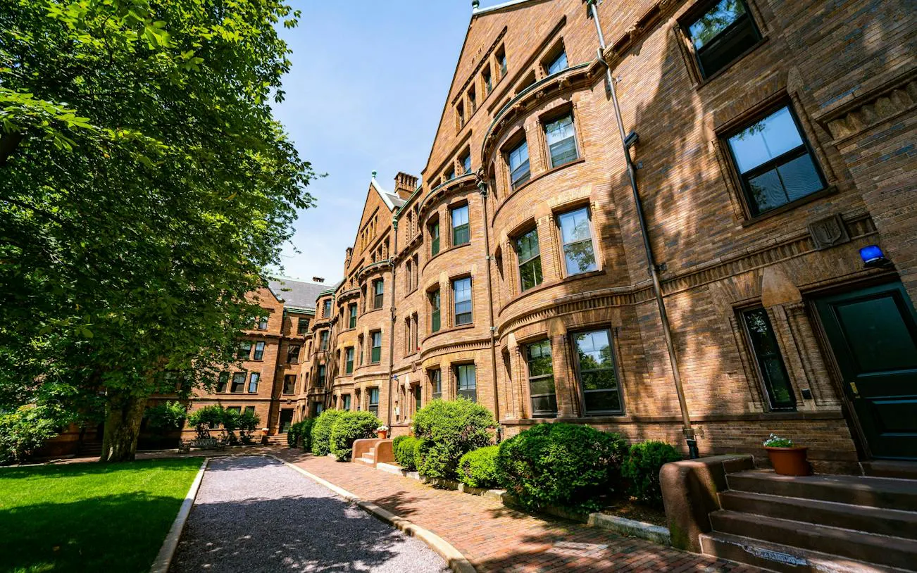 Historic brick building in Harvard Yard, Boston, surrounded by trees and a walkway.