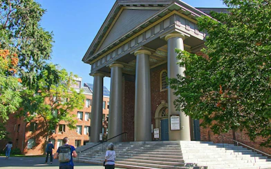 Harvard Yard building with columns and visitors, part of self-guided audio walk in Boston.