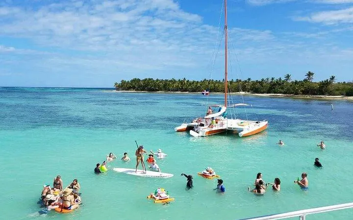 Punta Cana sailing cruise with people paddle boarding and snorkeling near a catamaran.