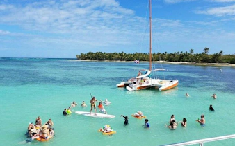 Punta Cana sailing cruise with people paddle boarding and snorkeling near a catamaran.