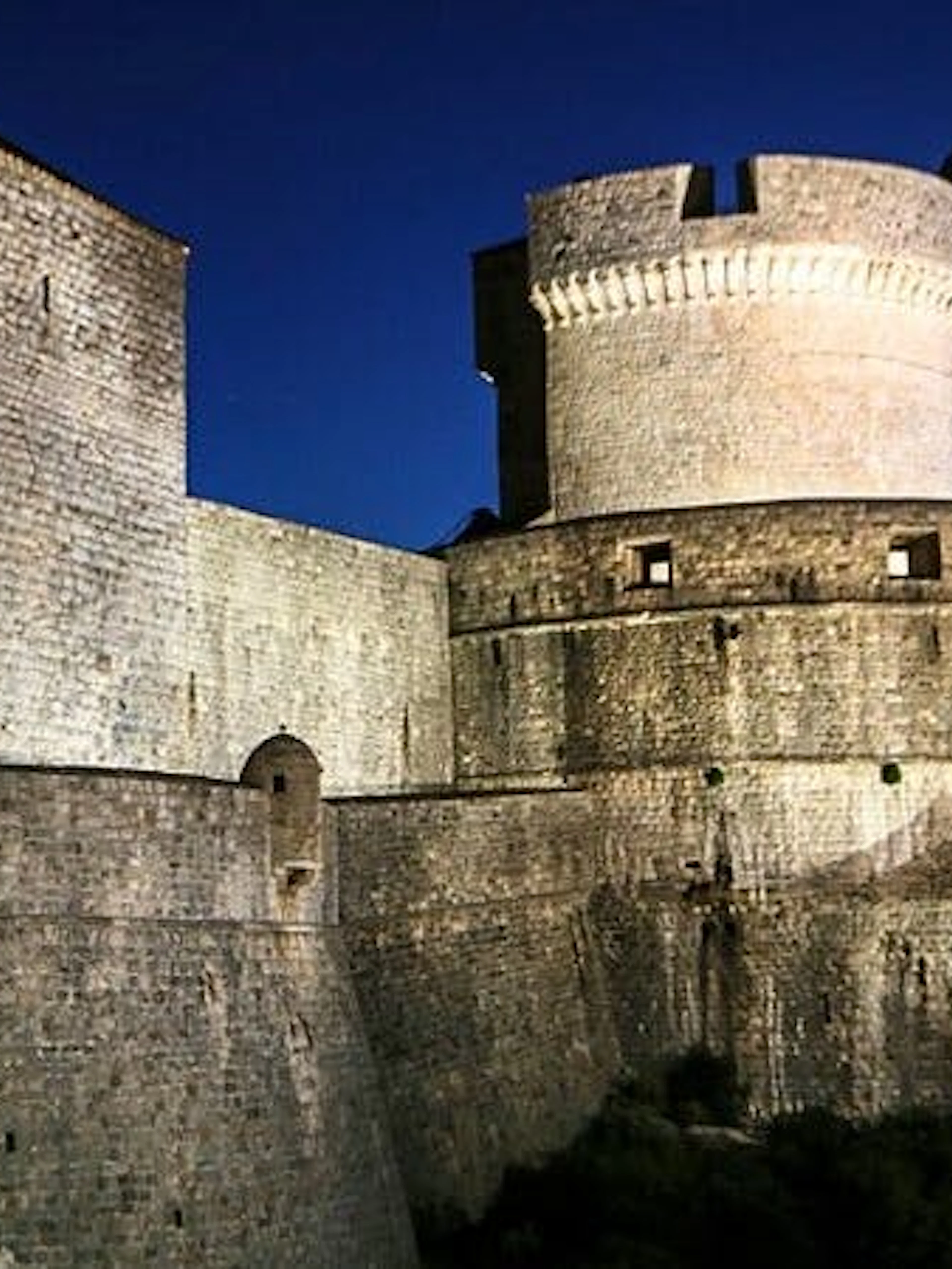 Dubrovnik city walls illuminated at night, featured in self-guided walking tour app.