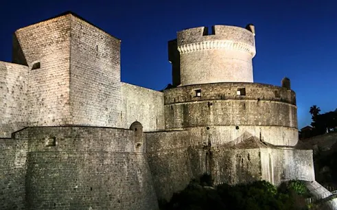 Dubrovnik city walls illuminated at night, featured in self-guided walking tour app.