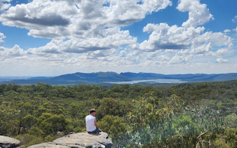 Hiker sitting on rock overlooking Grampians National Park landscape with mountains and clouds.