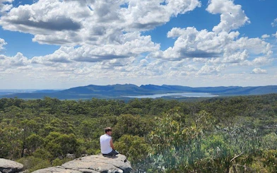 Hiker sitting on rock overlooking Grampians National Park landscape with mountains and clouds.