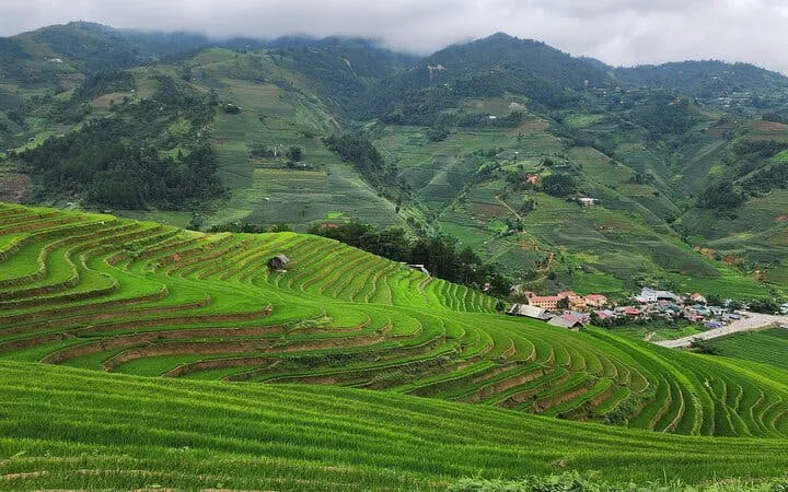 Terraced rice fields in Mu Cang Chai, Vietnam, with distant H’Mong village and lush green hills.