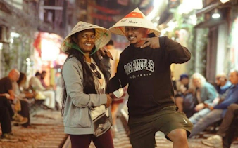 Tourists enjoying Hanoi E-Scooter City Tour with street food, wearing traditional hats.