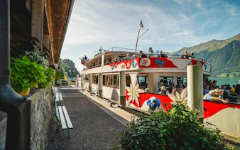 Boat docked at Lake Lucerne with passengers boarding, surrounded by mountains.