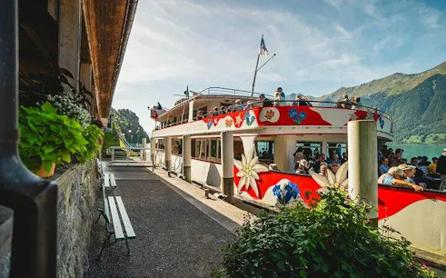 Boat docked at Lake Lucerne with passengers boarding, surrounded by mountains.