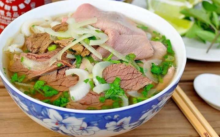 Pho noodle soup with beef slices, onions, and herbs in a decorative bowl.
