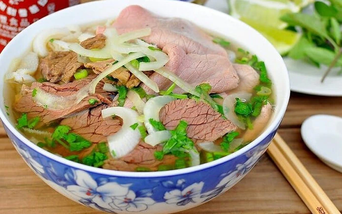 Pho noodle soup with beef slices, onions, and herbs in a decorative bowl.