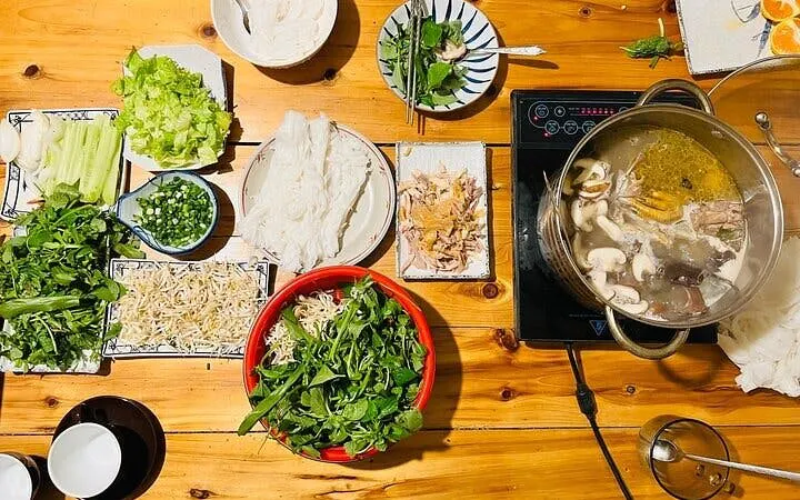 Pho noodle soup ingredients and cooking setup with herbs, noodles, and broth in a cooking class.