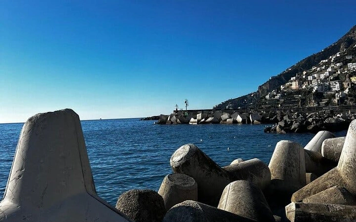 Rocky coastline of the Amalfi Coast with sea and hillside village in the background.