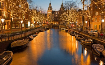 Amsterdam canal at dusk with illuminated trees and historic buildings, part of self-guided walking tour.