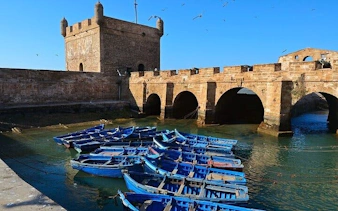 Essaouira harbor with blue fishing boats and historic fortress, part of Marrakesh day tour.
