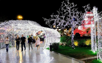 Visitors walking through illuminated tunnel at Soho Square, Sharm El Sheikh, with mosque in background.