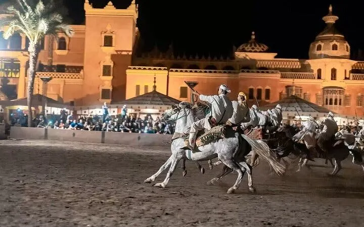 Riders performing at Chez-Ali Fantasia show in Marrakesh, with traditional Moroccan architecture in the background.