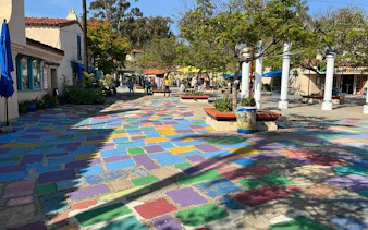 Colorful tiled walkway in Balboa Park, San Diego, with trees and people exploring nearby shops.