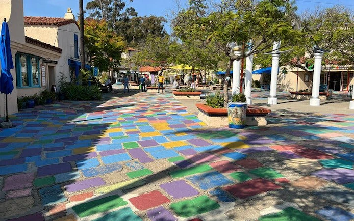 Colorful tiled walkway in Balboa Park, San Diego, with trees and people exploring nearby shops.