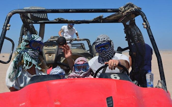 Buggy ride in Sharm El Sheikh desert during sunrise or sunset with passengers wearing scarves and goggles.