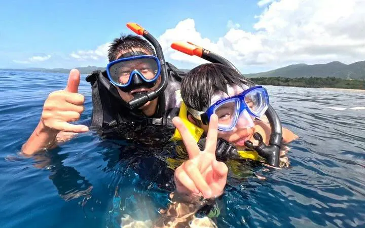Snorkelers enjoying Ishigaki Blue Cave waters, Okinawa, with Taketomi Island in the background.
