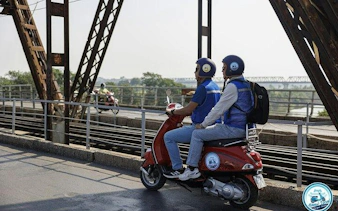 Two people riding a Vespa on Long Bien Bridge, Hanoi, during a half-day tour.