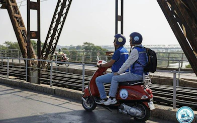 Two people riding a Vespa on Long Bien Bridge, Hanoi, during a half-day tour.
