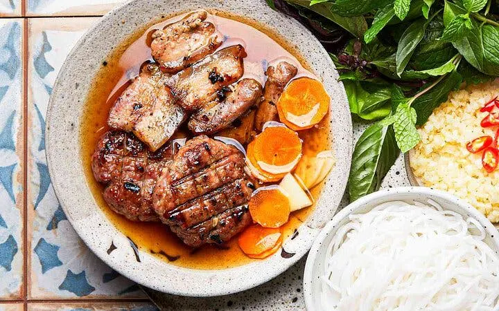 Bun Cha with grilled pork, noodles, herbs, and pickled vegetables in a Vietnamese cooking class setting.
