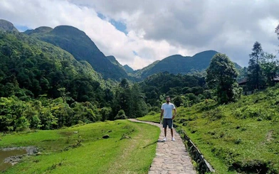 Sapa mountain path with traveler, lush greenery, and distant peaks.