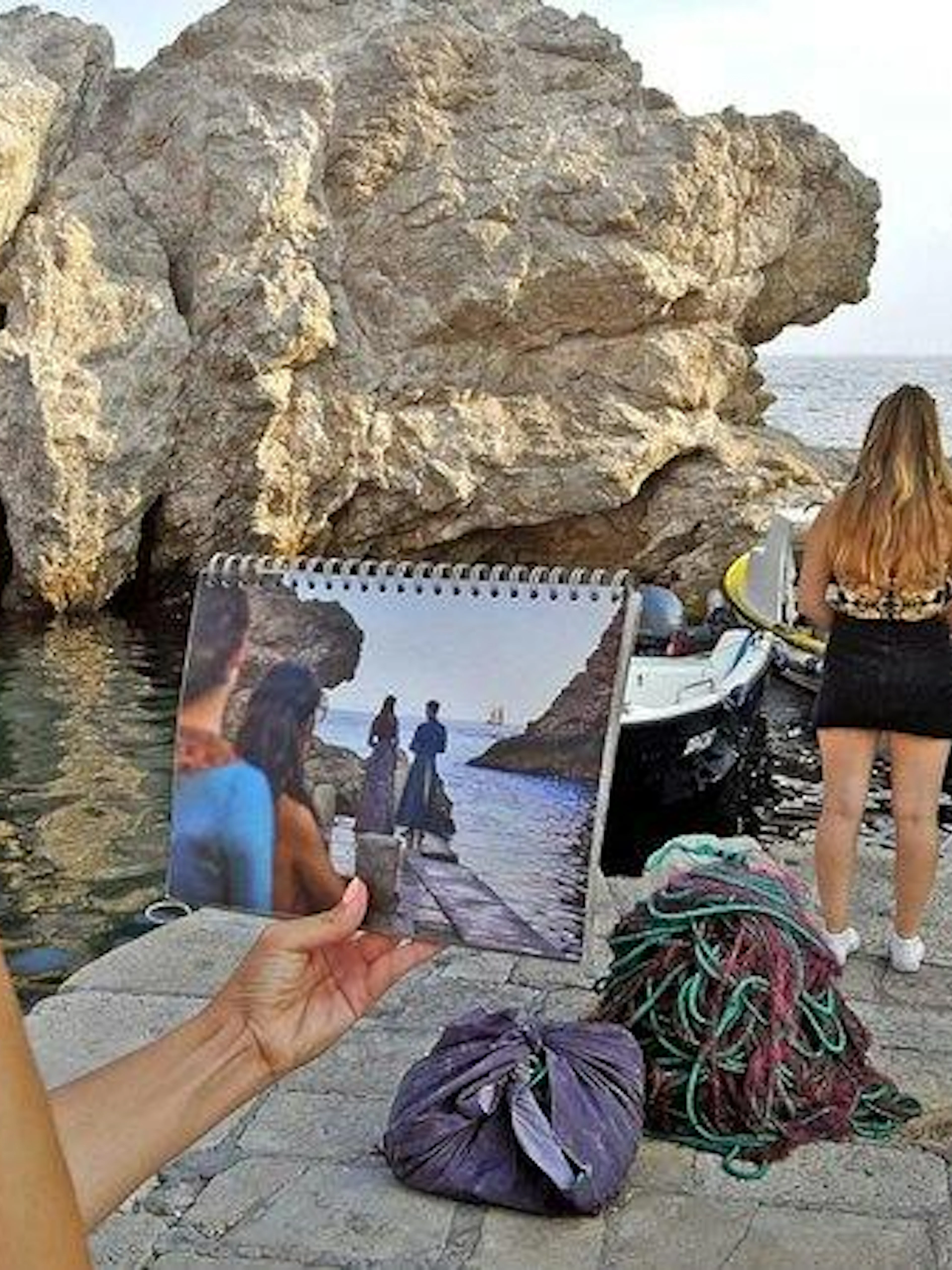 Tourists on Dubrovnik coast with Game of Thrones scene photo, near boats and rocky shore.