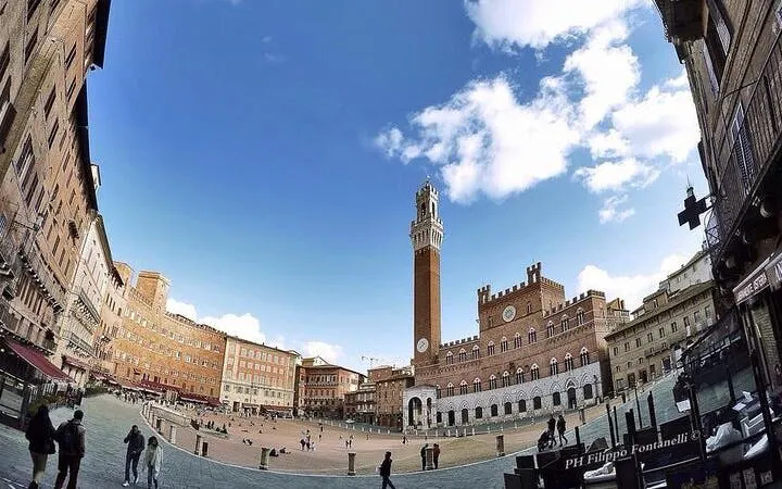 Piazza del Campo in Siena with Torre del Mangia under a blue sky.