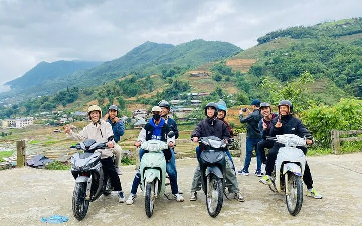 Motorbike riders in Sapa with scenic village and terraced hills in the background.