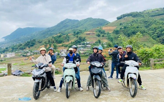 Motorbike riders in Sapa with scenic village and terraced hills in the background.