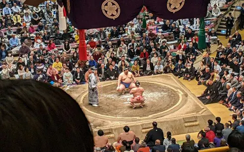 Sumo wrestlers competing in a Fukuoka arena with a large audience.