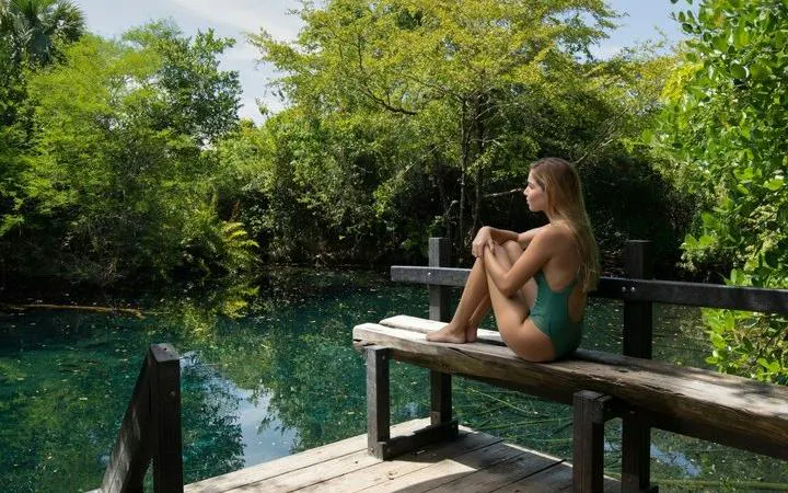 Woman sitting on a wooden deck by a cenote in Punta Cana, surrounded by lush greenery.