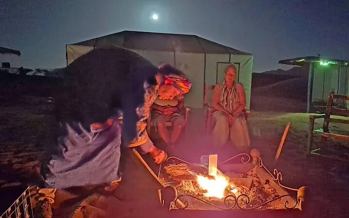 Campfire at Zagora desert camp with people sitting under moonlit sky, Marrakech camel trek.