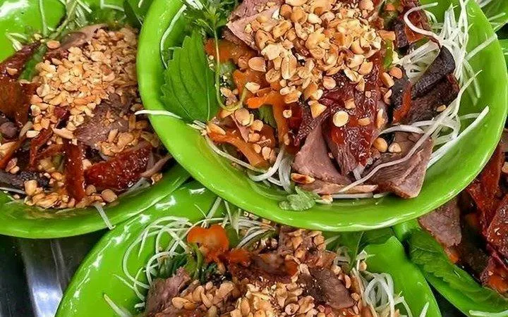 Hanoi street food dish with noodles, beef, herbs, and peanuts on green plates.