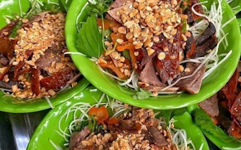 Hanoi street food dish with noodles, beef, herbs, and peanuts on green plates.