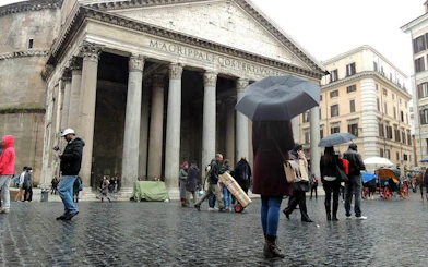 Pantheon in Rome with tourists exploring under umbrellas.