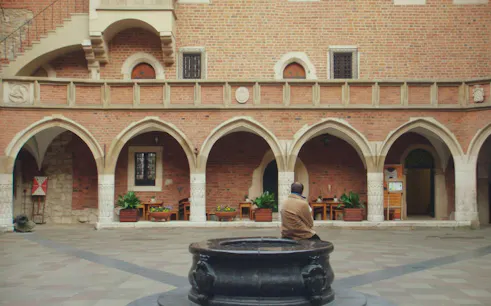 Courtyard with arches in Krakow Old Town, featuring a person sitting by a stone well.