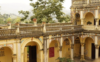 Ancient building with arched corridors at Bac Ha Market, Sapa, surrounded by lush greenery.